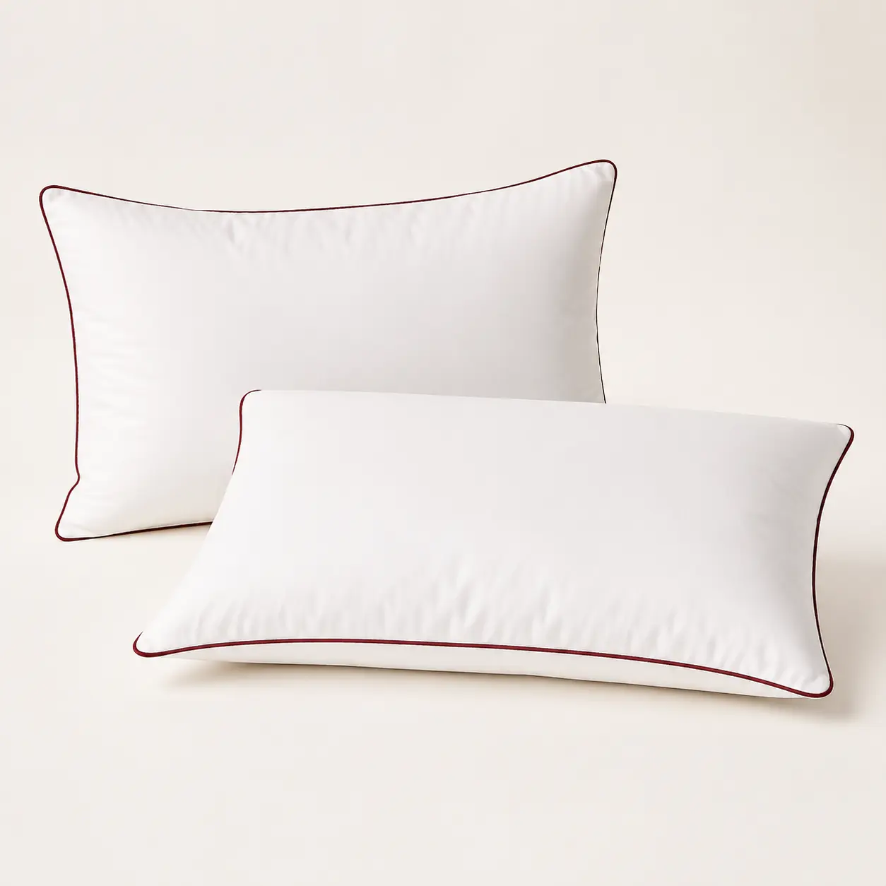 Two white pillows with wine-red piping on a studio background